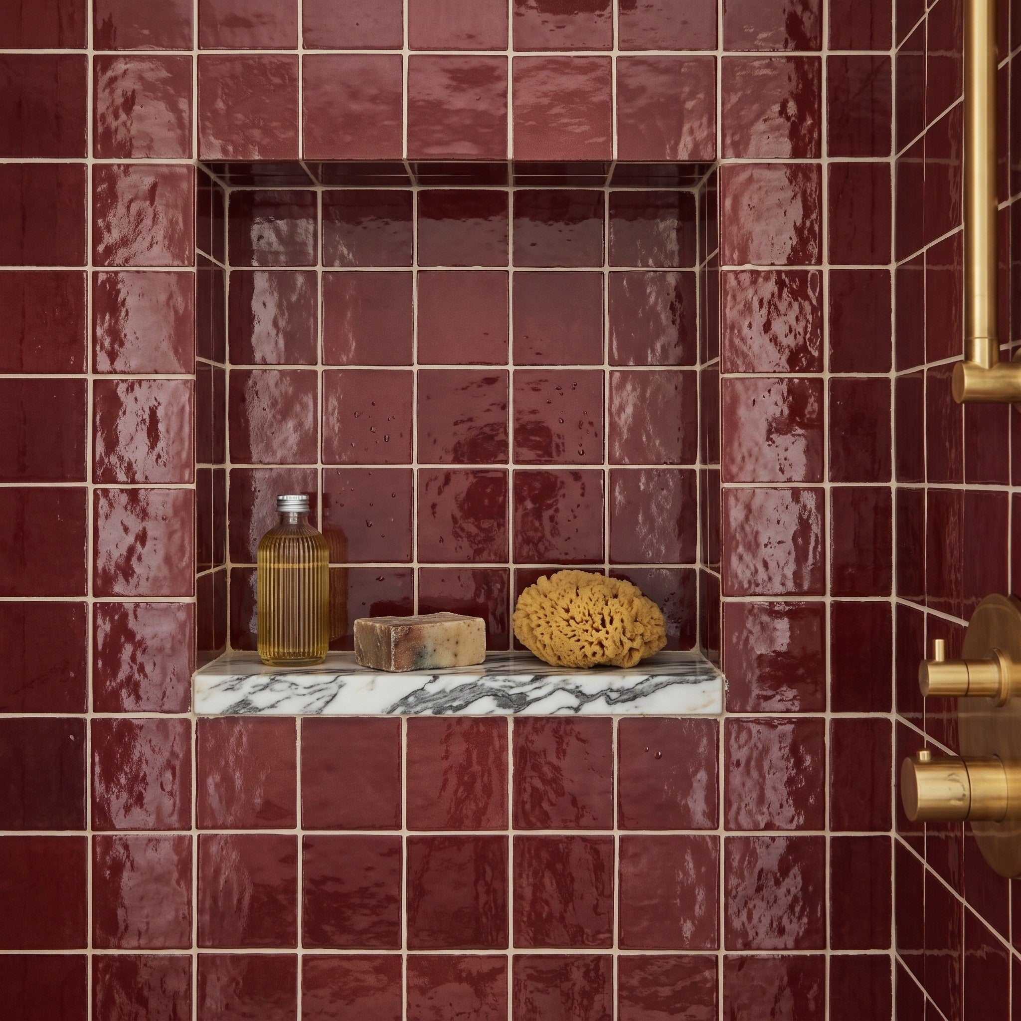 Fez Ruby wall tiles lining a shower niche with a marble shelf, glossy deep red glaze, brass shower valve visible at right.
