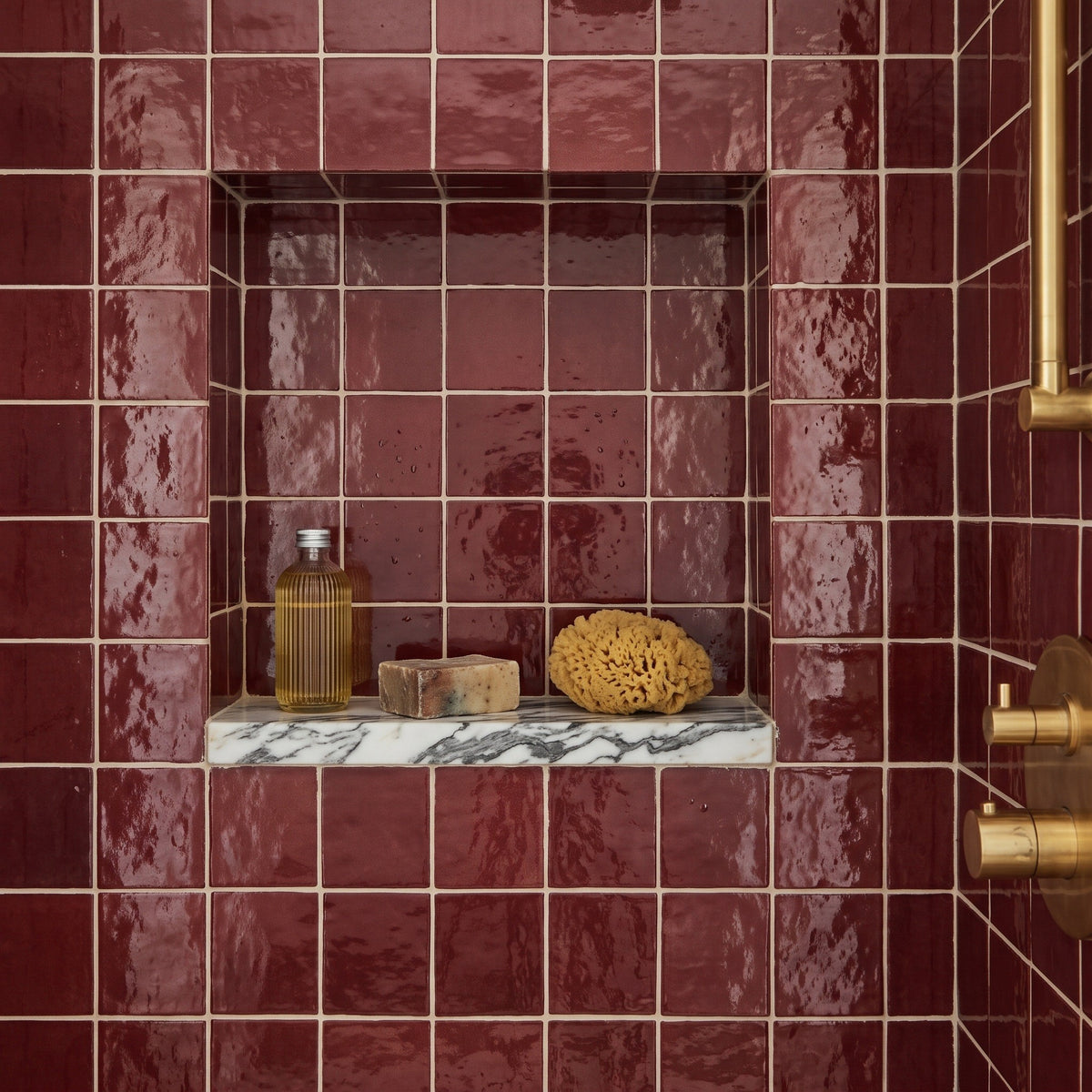 Fez Ruby wall tiles lining a shower niche with a marble shelf, glossy deep red glaze, brass shower valve visible at right.
