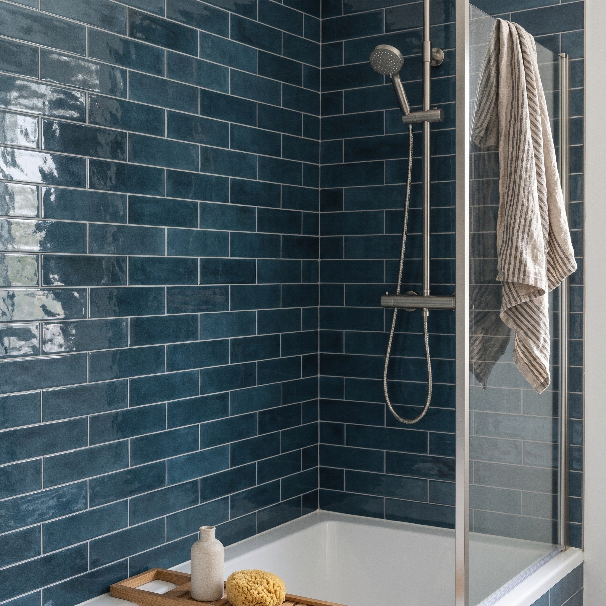 Opal Marine wall tiles lining a shower bath corner in a running bond pattern, with a glass screen, chrome shower riser and